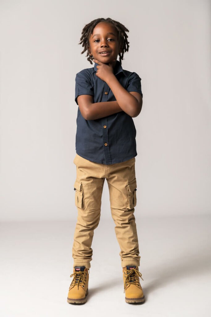 un petit garçon de couleur habillé d'un pantalon de couleur camel et d'une petit chemisette bleue