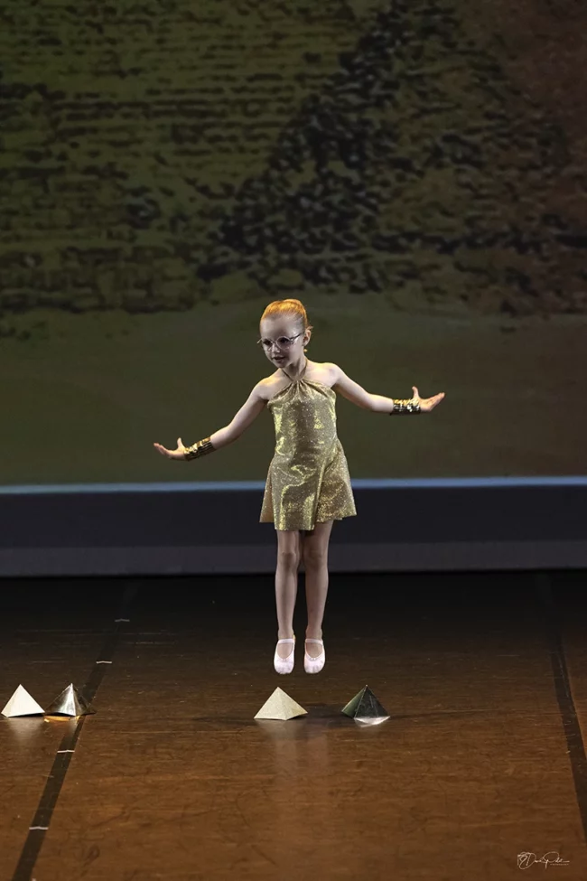 Jeune danseuse en costume pailleté or sautant devant des pyramides lors du spectacle