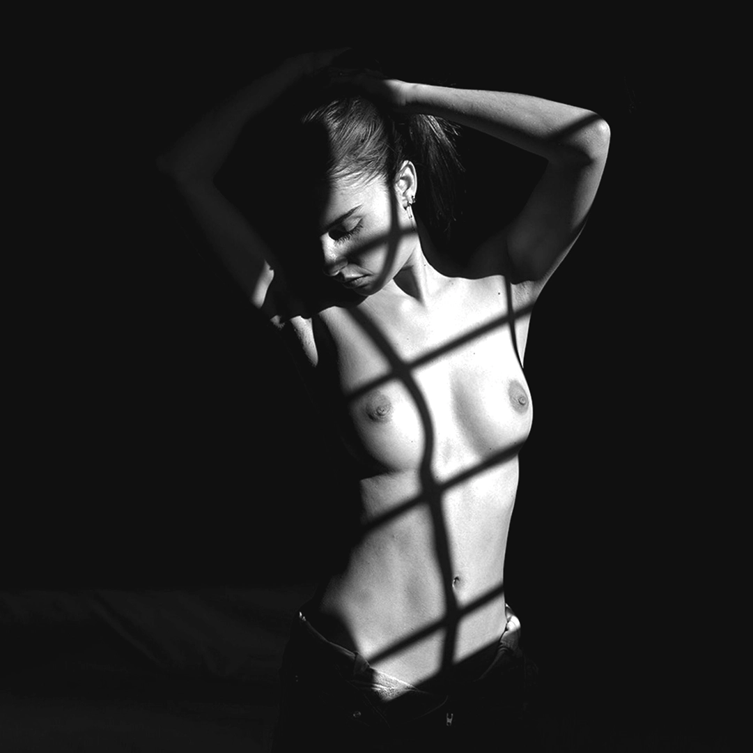 shoot-photo-nu-art-03 Femme torse nu, une grille projetant une ombre sur sa poitrine. Photographie par David Polet Photography à Nice et Villeneuve-Loubet