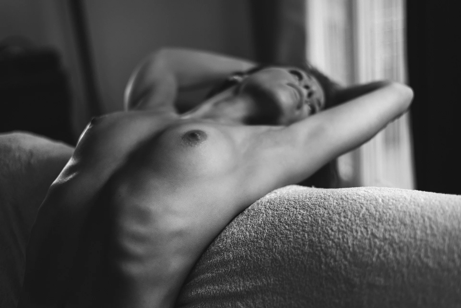 shoot-photo-nu-art-11 Femme allongée, torse nu, capturée dans une pose sensuelle en noir et blanc, baignée d’une lumière douce.