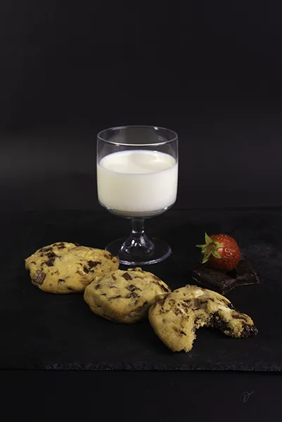 Cookies aux pépites de chocolat avec verre de lait, photographie culinaire sur fond noir, dessert gourmand.