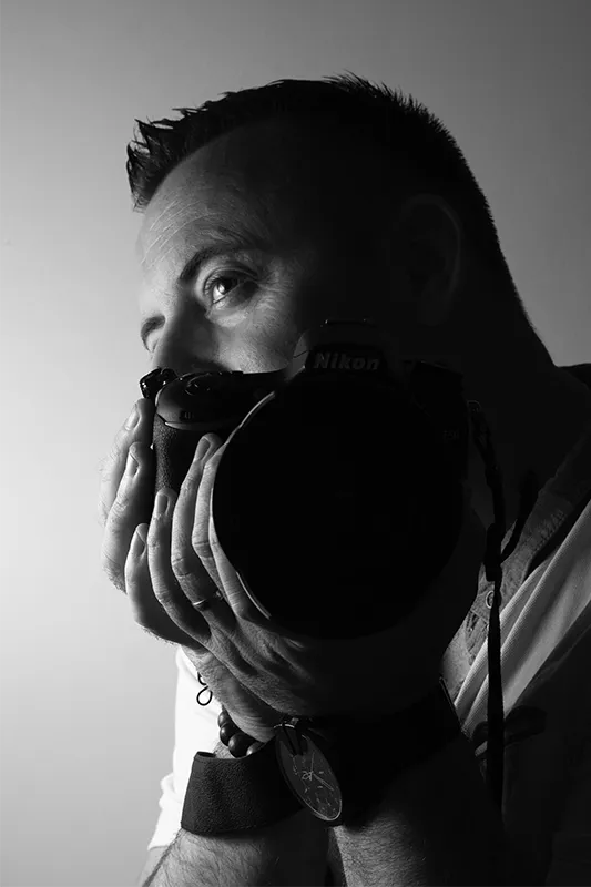 Portrait noir et blanc d’un photographe tenant un appareil photo, regard intense en studio – Photographe Villeneuve Loubet