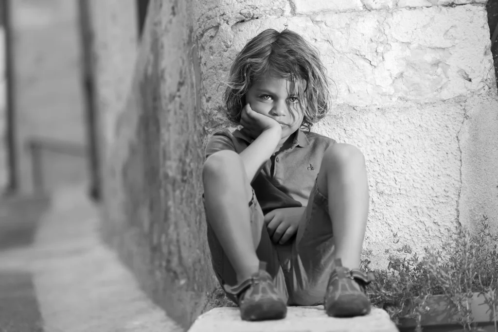 Portrait en noir et blanc d’un enfant assis contre un mur lors d’une séance photo enfant Nice.