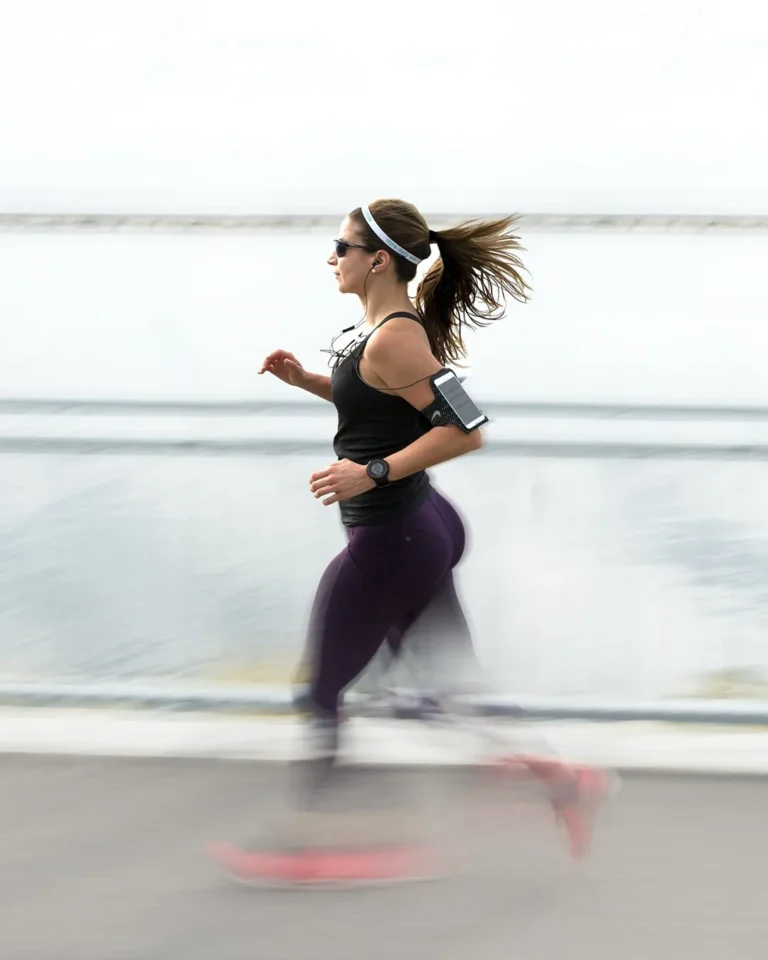 Femme en tenue de sport courant sur une promenade en bord de mer, écouteurs et brassard smartphone