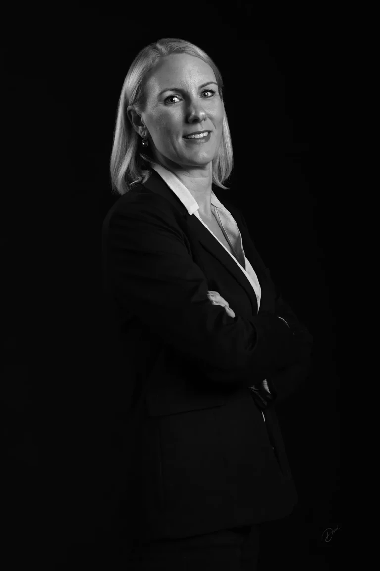 Portrait corporate noir et blanc en studio, femme en tailleur bras croisés sur fond noir, lumière douce et rendu premium
