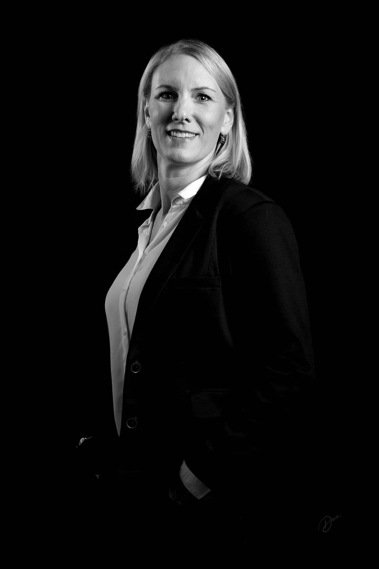 Portrait corporate professionnel d’une femme en costume noir, fond noir, photographie d’entreprise élégante.