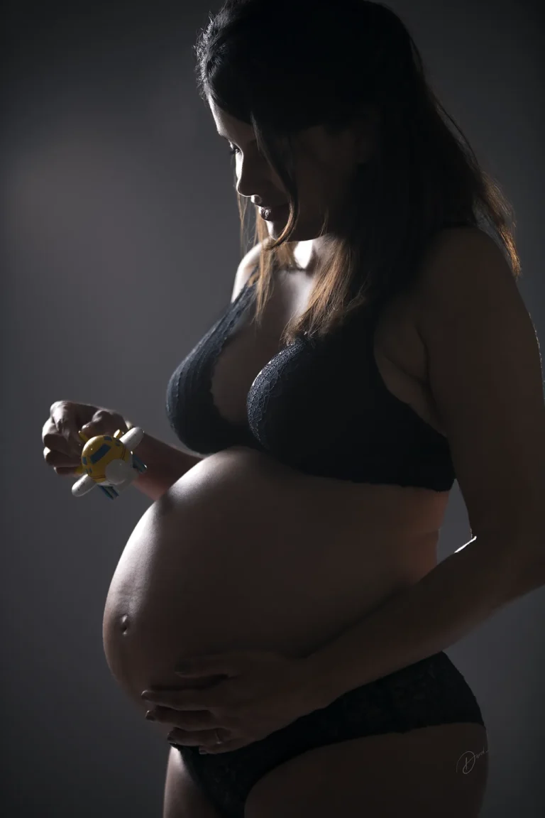 Femme enceinte en studio en clair-obscur, tenant un jouet