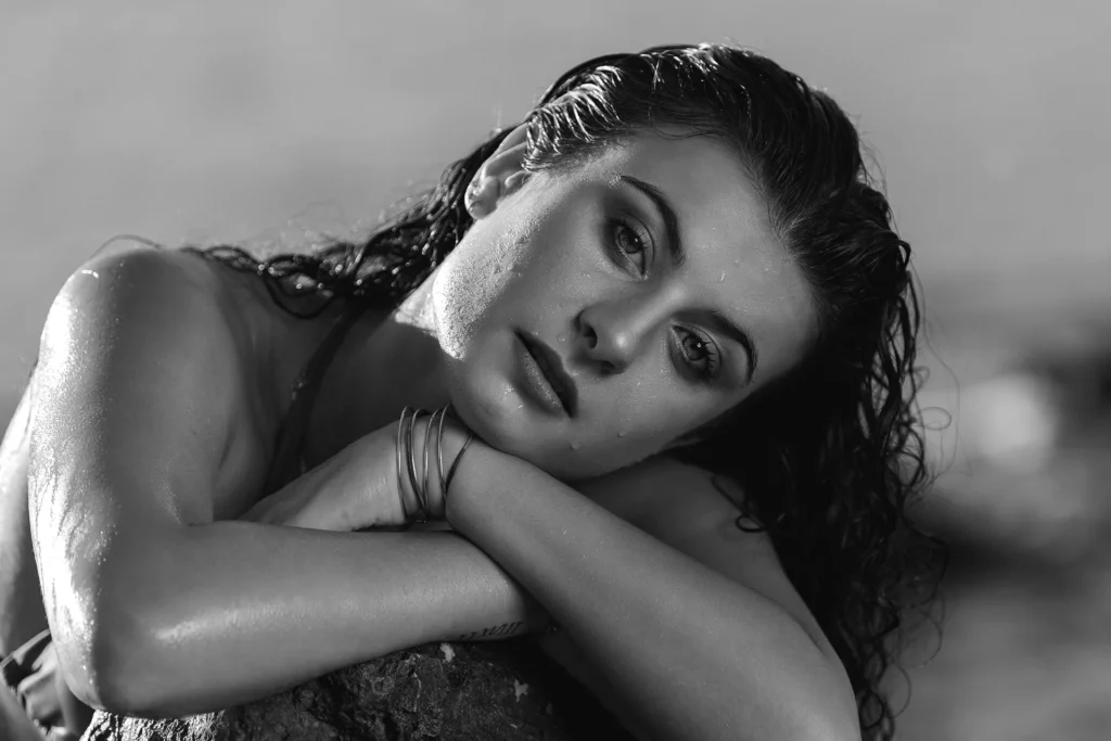 Portrait noir et blanc d’une modèle aux cheveux mouillés, allongée sur un rocher au bord de mer