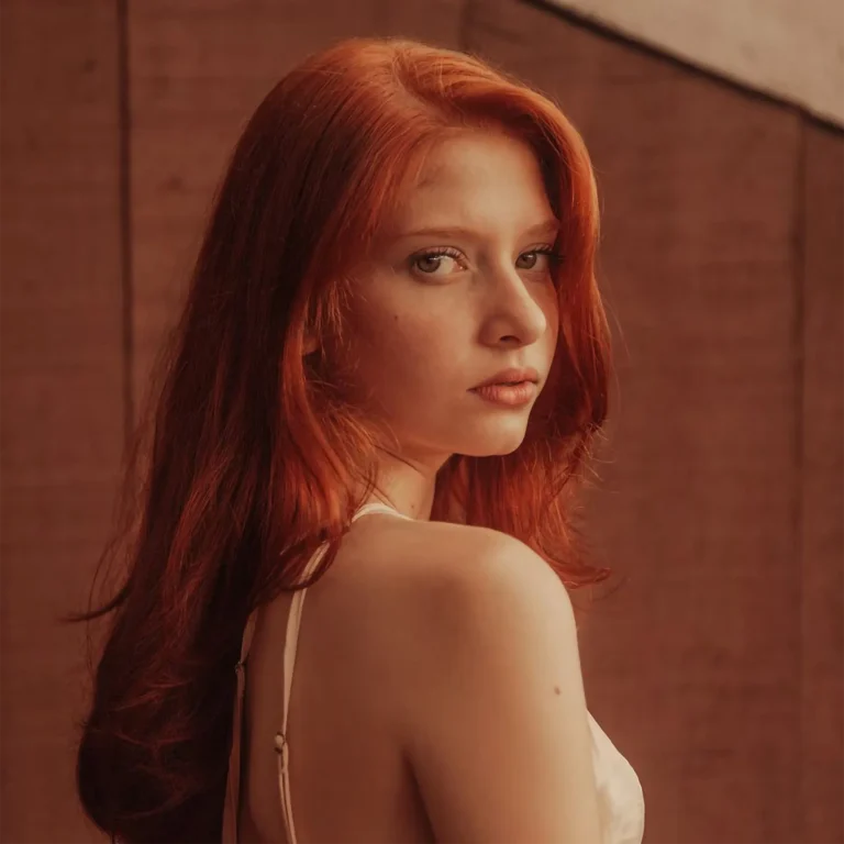 Portrait mode d’une femme rousse en lumière chaude, regard caméra, arrière-plan minimaliste