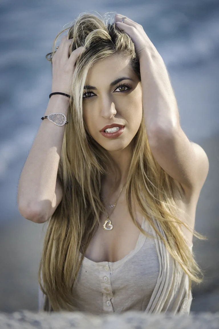 Portrait lifestyle Côte d’Azur : femme blonde au regard intense, mains dans les cheveux, fond mer